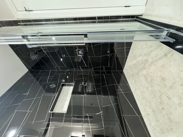 Black marble-look porcelain shower with a mosaic band and a linear drain